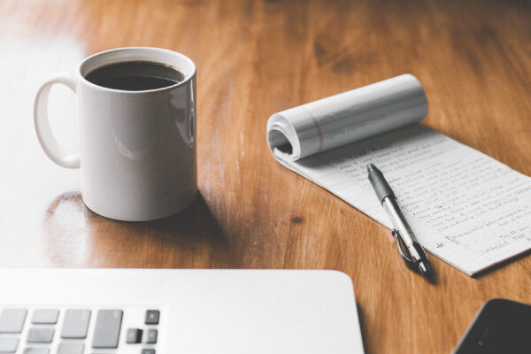 Remote workspace with featuring a laptop, a cup of coffee, a pen, and a notepad